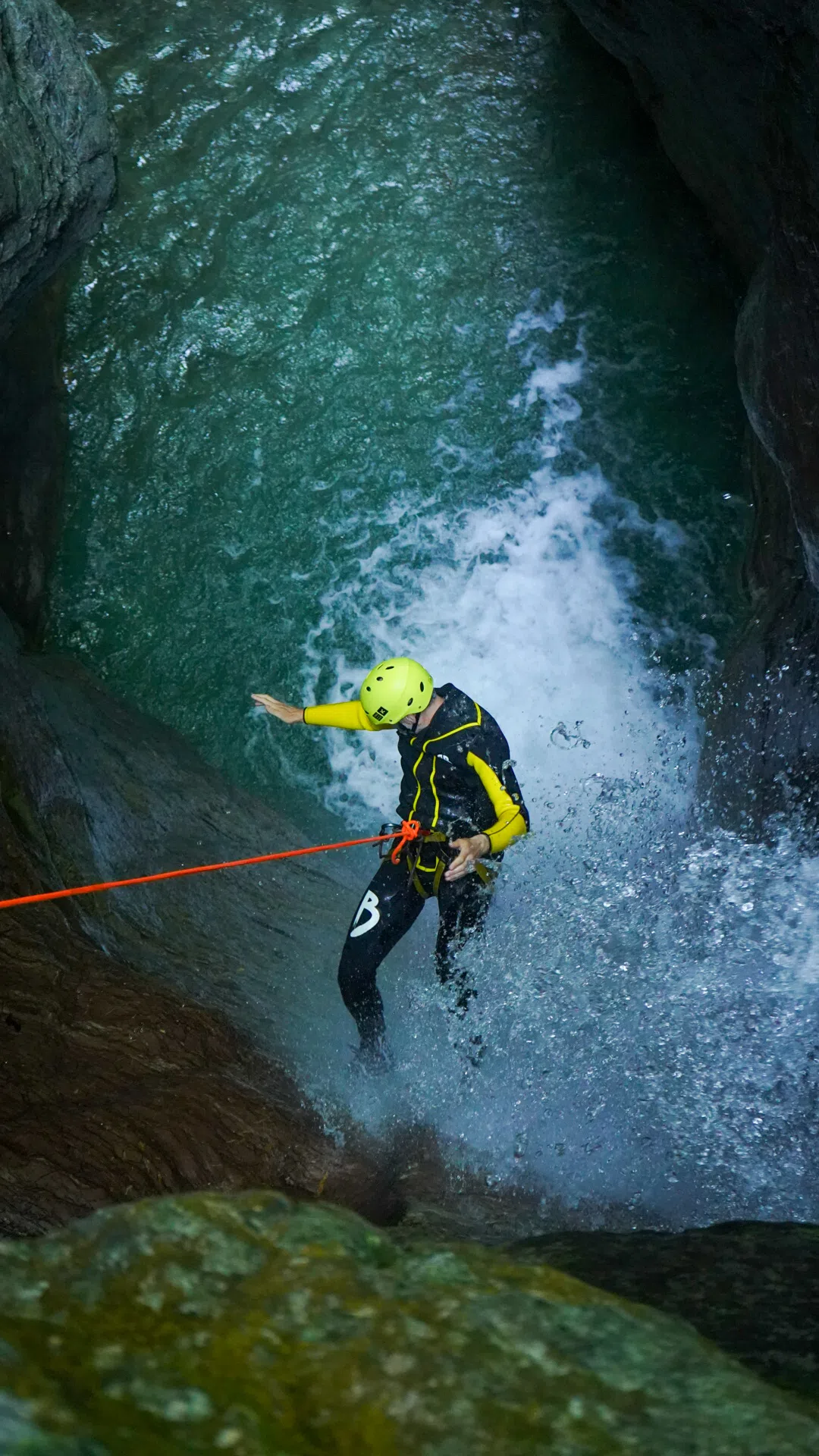 Canyoning participant descending beside a waterfall into a pool