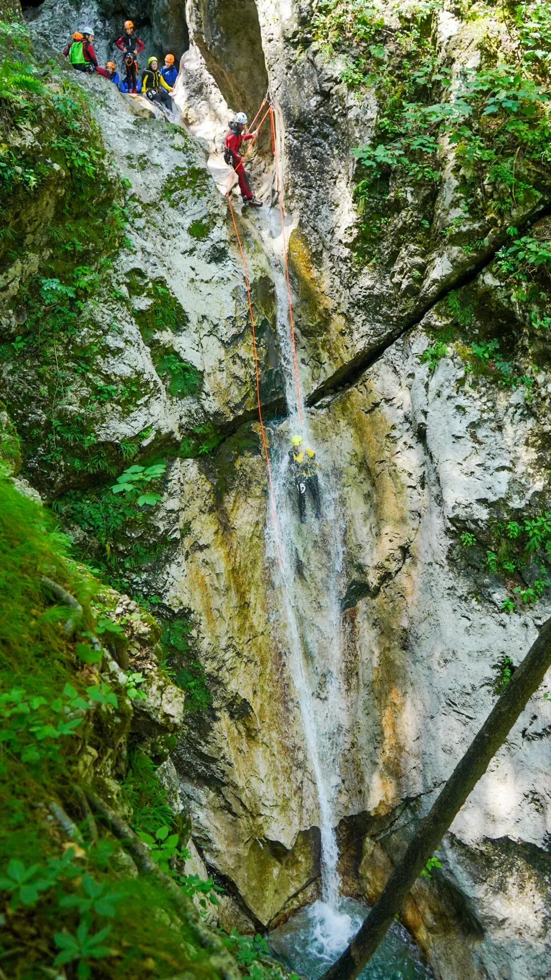 Canyoning participant descending a waterfall between steep rock walls in the Soča Valley.