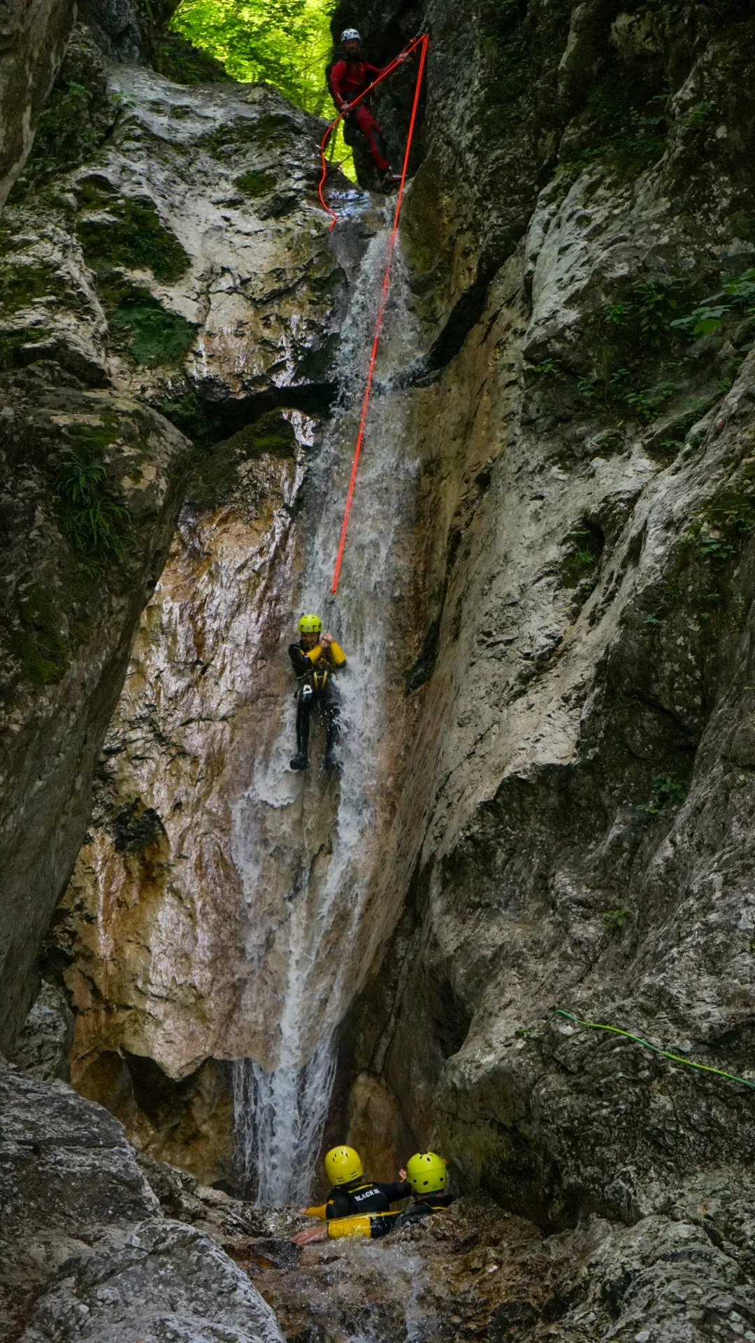 Canyoning participant rappelling down a waterfall in a narrow gorge in the Soča Valley.