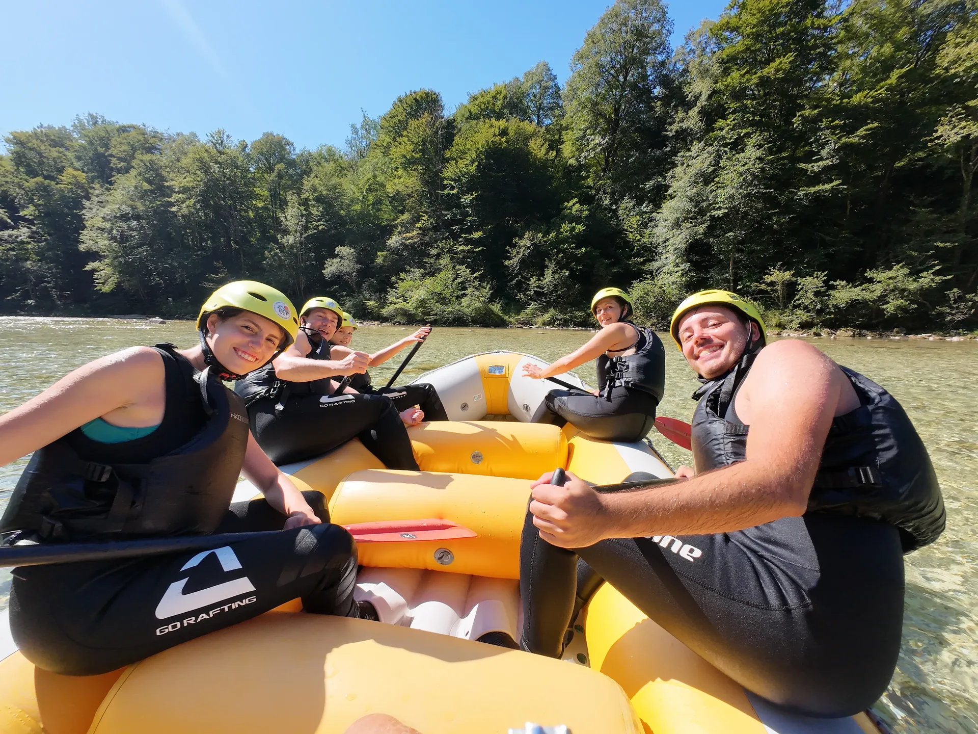 Smiling guests sitting in a yellow raft beside the Soča River before their rafting adventure.