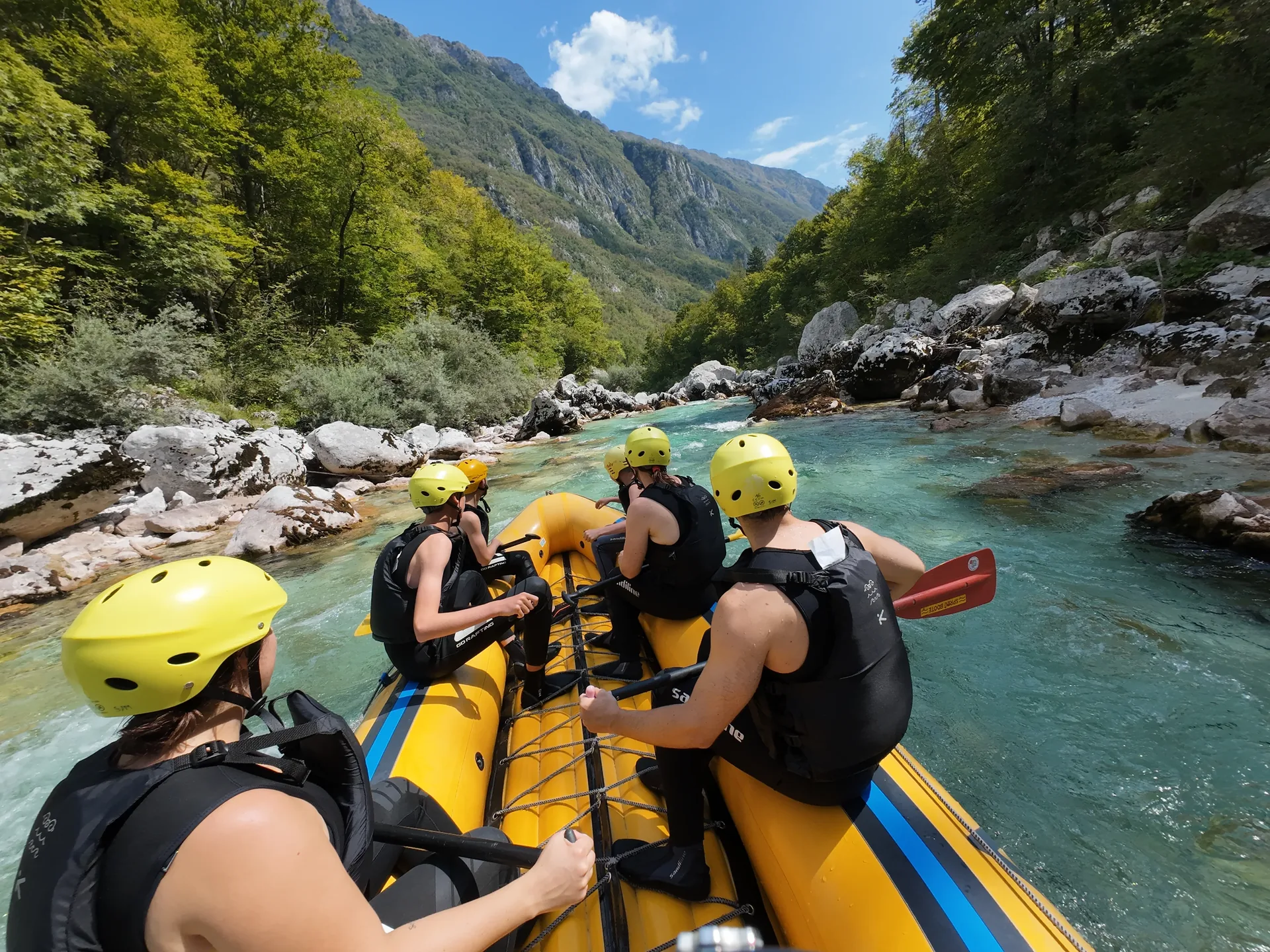 Rafting group paddling through the turquoise Soča River surrounded by mountains and forest.