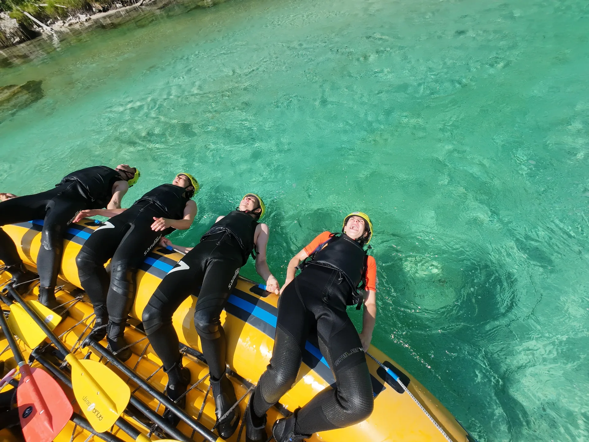 Rafting guests relaxing on a yellow raft in the clear turquoise water of the Soča River.