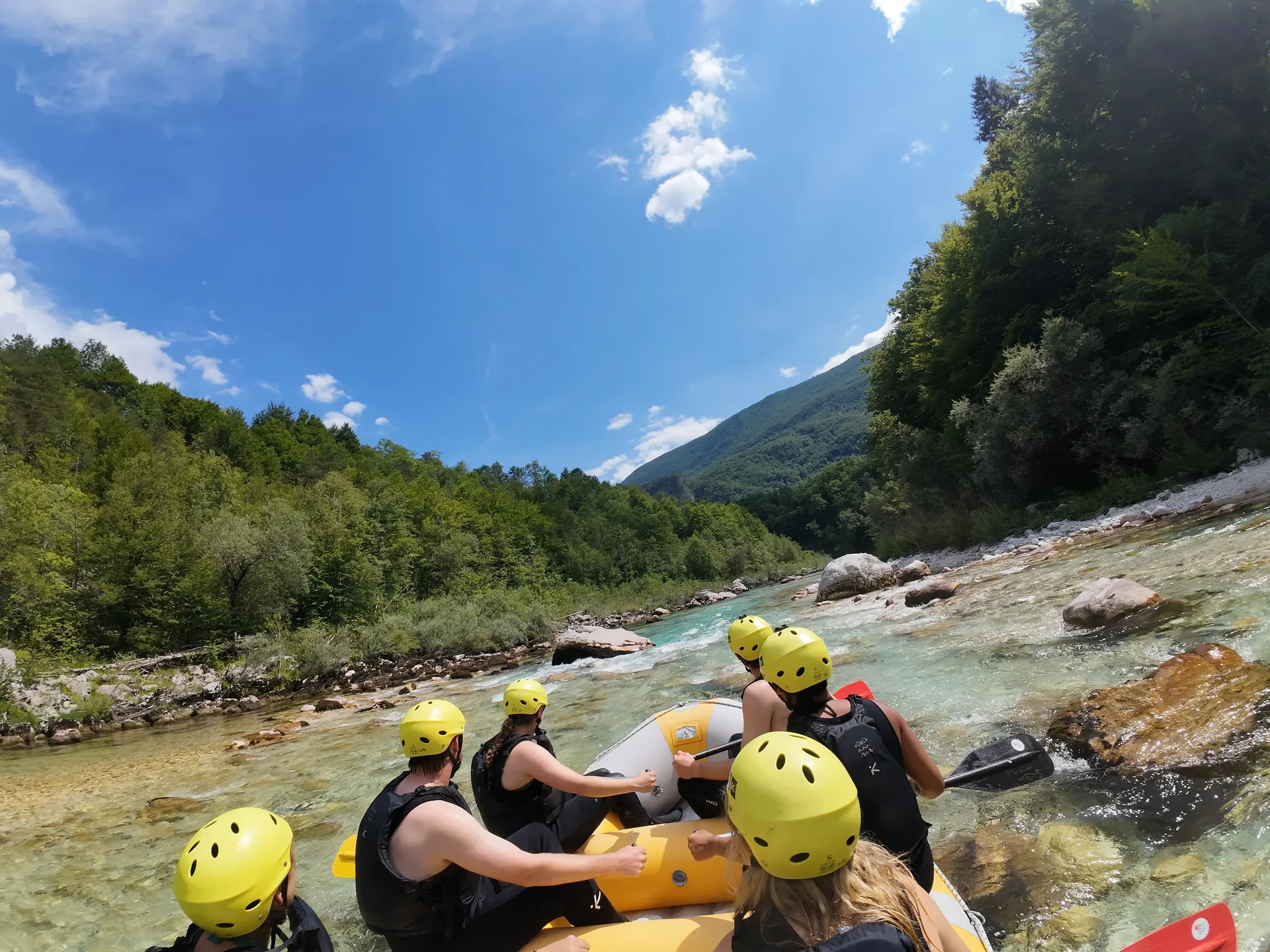 View from a raft with guests on the clear Soča River surrounded by the mountains of the Soča Valley.